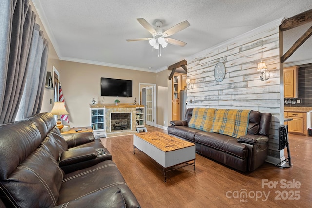 living room with a tile fireplace, wood-type flooring, ornamental molding, ceiling fan, and a textured ceiling