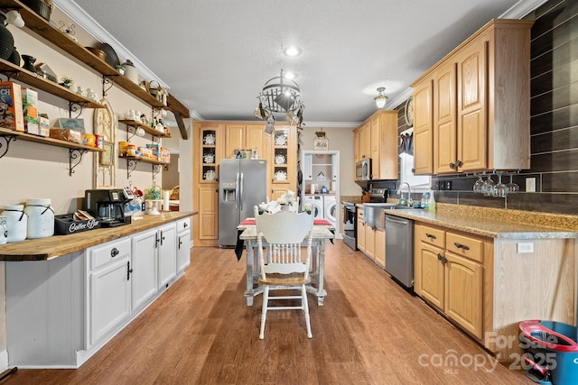 kitchen featuring butcher block countertops, crown molding, stainless steel appliances, washing machine and dryer, and light hardwood / wood-style flooring