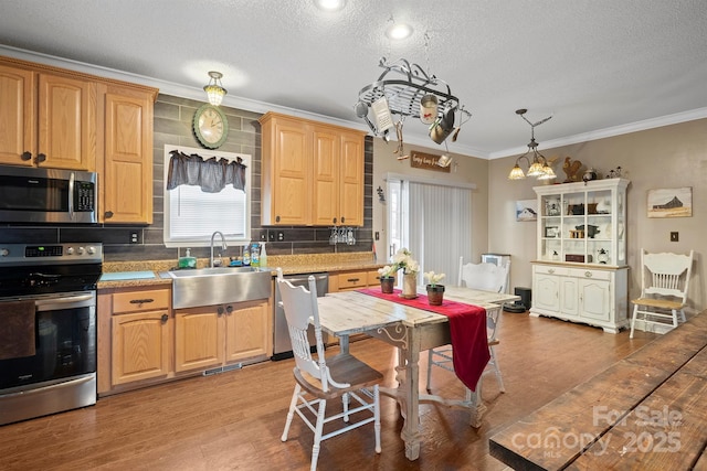 kitchen featuring sink, crown molding, hanging light fixtures, stainless steel appliances, and light hardwood / wood-style floors