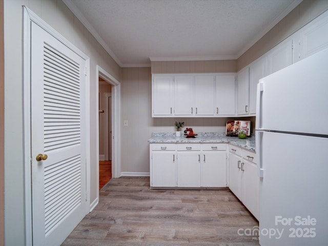 kitchen featuring light wood-type flooring, white refrigerator, ornamental molding, light stone countertops, and white cabinets