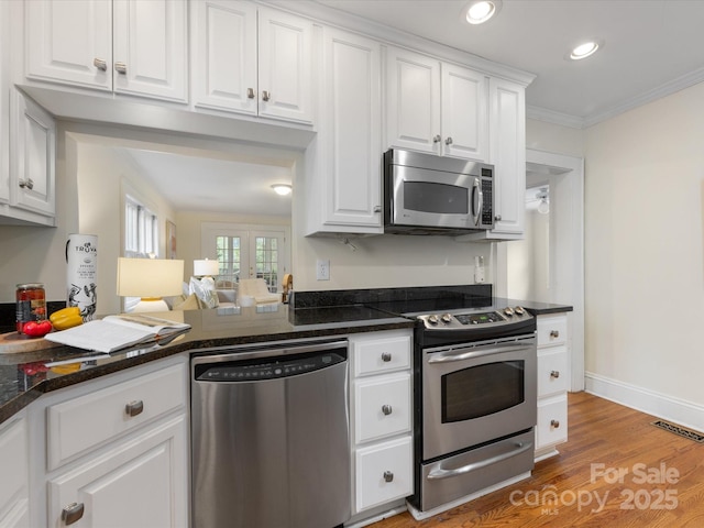 kitchen with white cabinets, dark stone counters, ornamental molding, stainless steel appliances, and light wood-type flooring