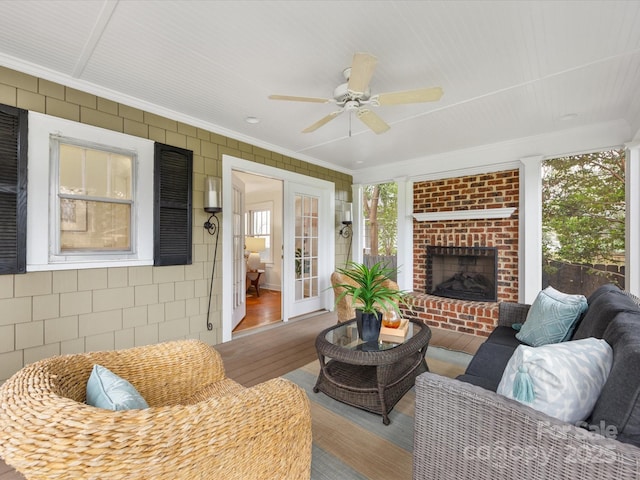 living room featuring wood-type flooring, ceiling fan, crown molding, a brick fireplace, and french doors