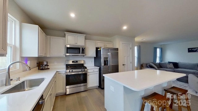 kitchen featuring appliances with stainless steel finishes, a breakfast bar, white cabinetry, sink, and light hardwood / wood-style flooring