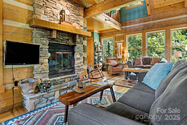 living room featuring wood-type flooring, a stone fireplace, a towering ceiling, and wooden walls