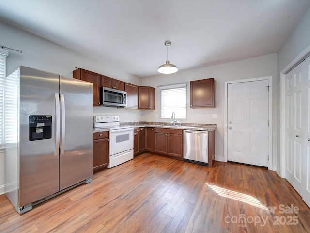 kitchen with stainless steel appliances, light hardwood / wood-style floors, sink, and hanging light fixtures