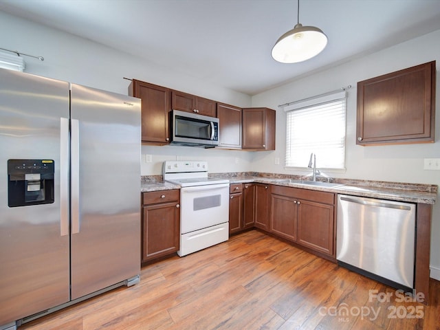 kitchen featuring pendant lighting, sink, light stone counters, stainless steel appliances, and light wood-type flooring