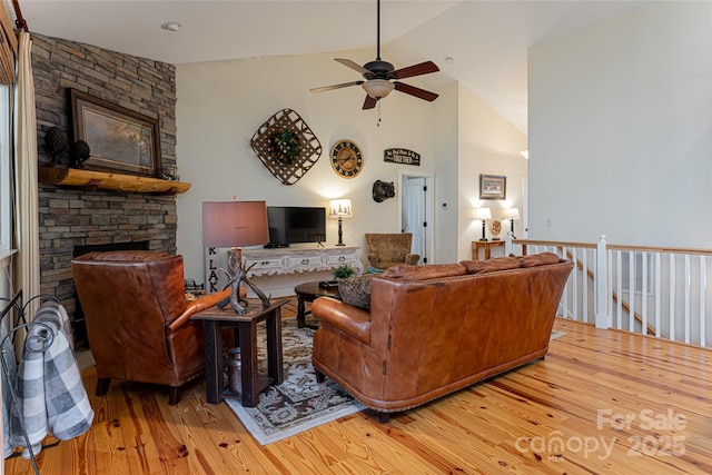 living room featuring ceiling fan, high vaulted ceiling, a fireplace, and light hardwood / wood-style floors