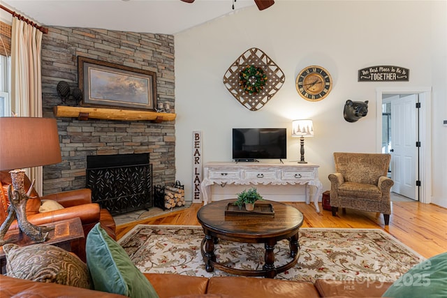 living room with lofted ceiling, hardwood / wood-style floors, a stone fireplace, and ceiling fan