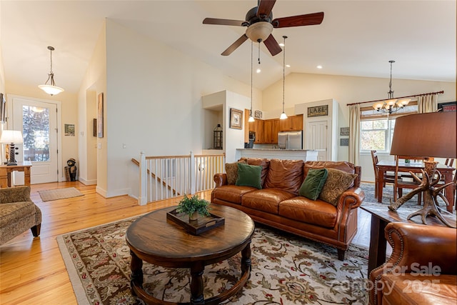 living room with ceiling fan with notable chandelier, high vaulted ceiling, and light wood-type flooring