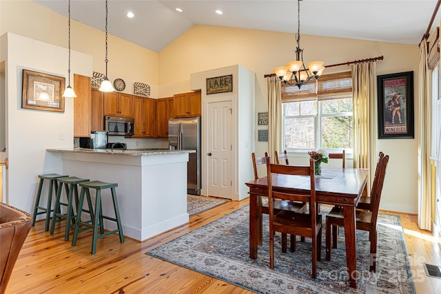 kitchen with a kitchen bar, hanging light fixtures, light wood-type flooring, appliances with stainless steel finishes, and kitchen peninsula