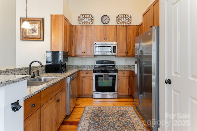 kitchen with sink, light stone counters, light wood-type flooring, appliances with stainless steel finishes, and pendant lighting