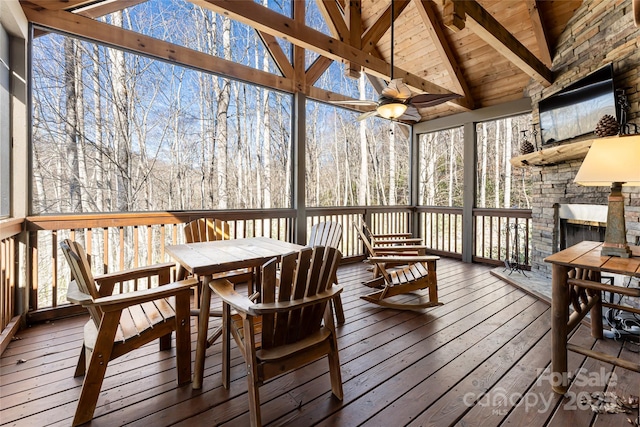 sunroom with lofted ceiling with beams, ceiling fan, wood ceiling, and an outdoor stone fireplace