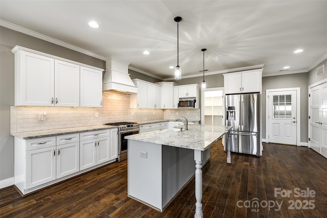 kitchen with stainless steel appliances, premium range hood, white cabinetry, light stone countertops, and decorative light fixtures