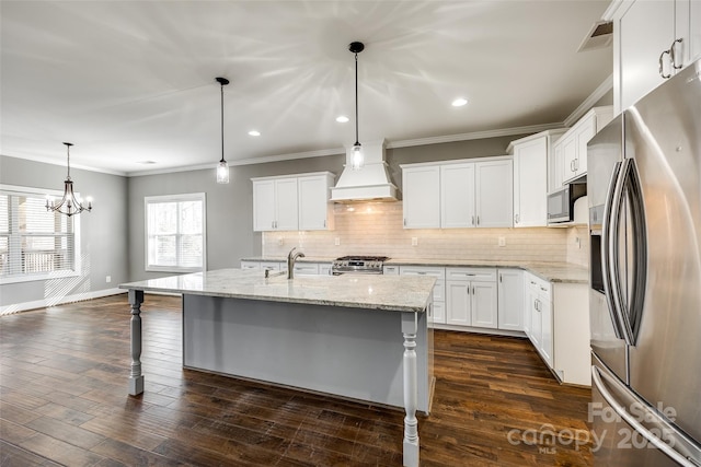 kitchen with a kitchen island with sink, white cabinets, appliances with stainless steel finishes, decorative light fixtures, and custom range hood