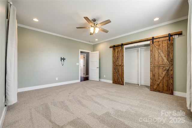 unfurnished bedroom featuring carpet, recessed lighting, a barn door, ornamental molding, and baseboards