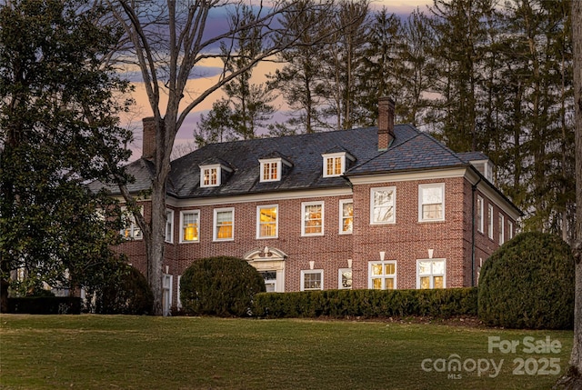 colonial home with a high end roof, brick siding, a yard, and a chimney