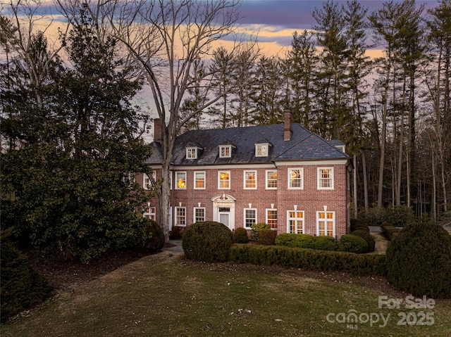 colonial house with brick siding, a lawn, a chimney, and a high end roof