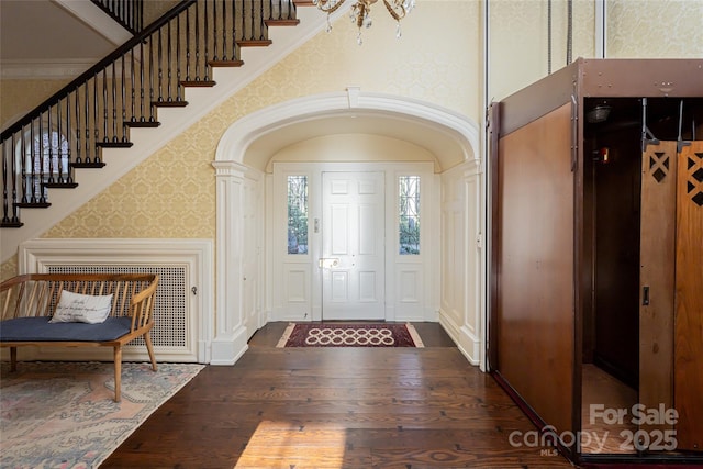 foyer entrance featuring wallpapered walls, arched walkways, dark wood-style flooring, a high ceiling, and crown molding