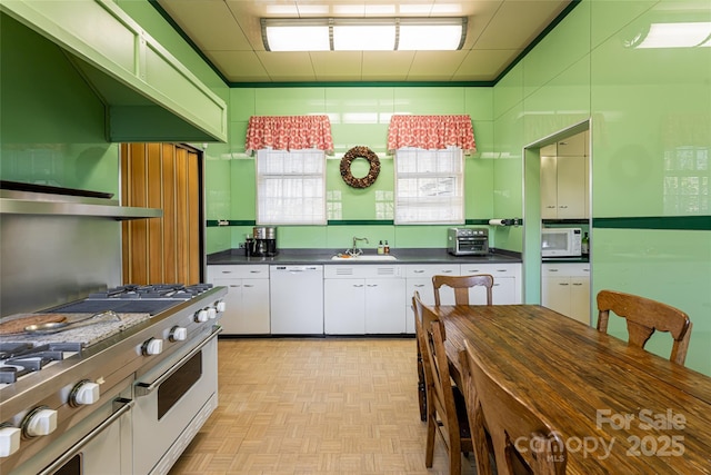 kitchen featuring dark countertops, white appliances, white cabinets, and a sink