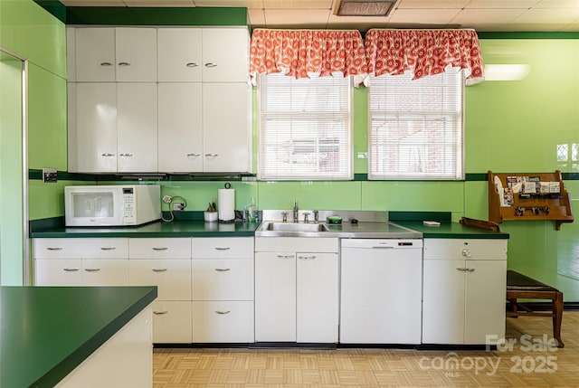 kitchen featuring dark countertops, white appliances, white cabinetry, and a sink