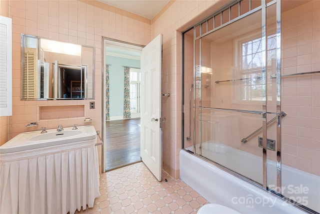 bathroom with tile walls, vanity, and bath / shower combo with glass door