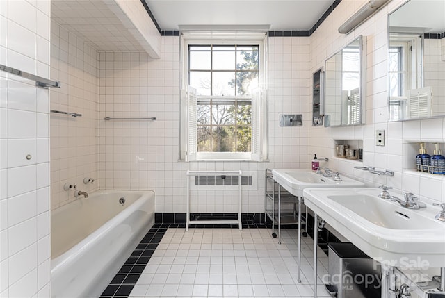 bathroom with two sinks, a garden tub, tile patterned flooring, tile walls, and radiator heating unit