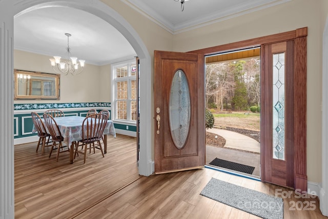 foyer entrance featuring ornamental molding, a chandelier, a wealth of natural light, and wood finished floors