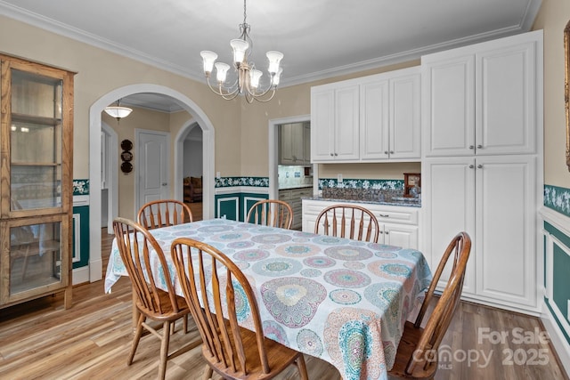 dining space featuring arched walkways, light wood finished floors, an inviting chandelier, and crown molding