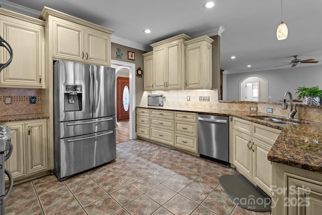 kitchen with cream cabinets, appliances with stainless steel finishes, arched walkways, and a sink