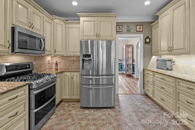 kitchen featuring light tile patterned floors, cream cabinets, appliances with stainless steel finishes, light stone countertops, and crown molding