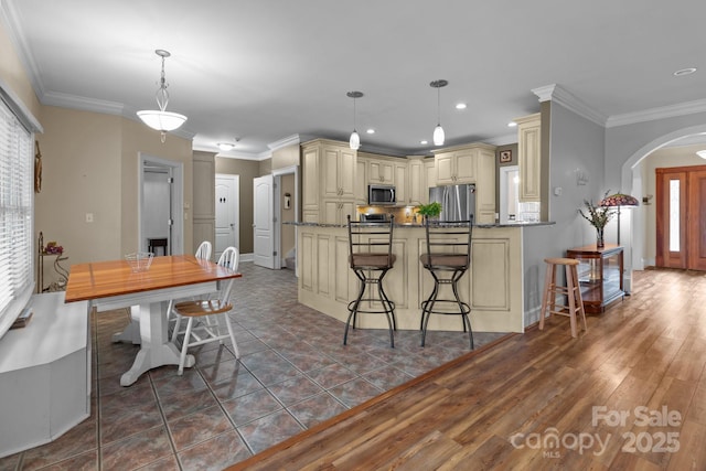 kitchen featuring arched walkways, cream cabinetry, crown molding, stainless steel appliances, and a peninsula