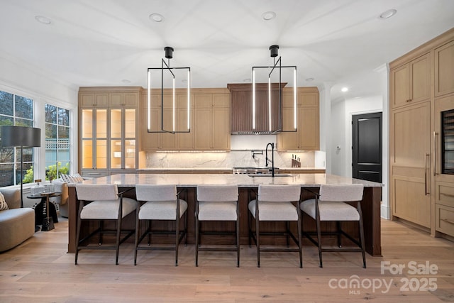 kitchen featuring a breakfast bar, decorative light fixtures, backsplash, a center island with sink, and wall chimney exhaust hood