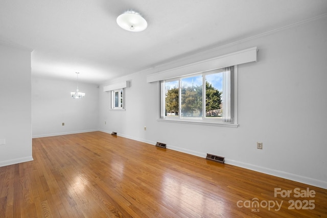 spare room with baseboards, visible vents, a chandelier, and wood finished floors