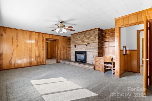 unfurnished living room with wood walls, crown molding, carpet flooring, and a stone fireplace