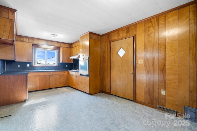 kitchen with brown cabinetry, dark countertops, oven, and under cabinet range hood