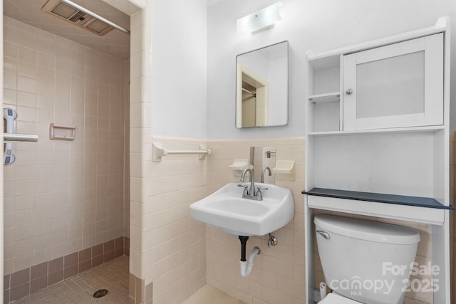 bathroom featuring a wainscoted wall, visible vents, toilet, a tile shower, and a sink