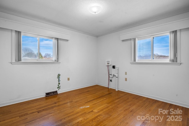 spare room with a healthy amount of sunlight, visible vents, a textured ceiling, and wood finished floors