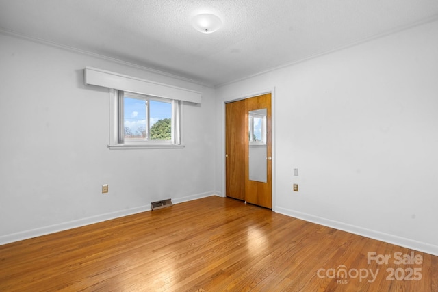 spare room with baseboards, a textured ceiling, visible vents, and light wood-style floors