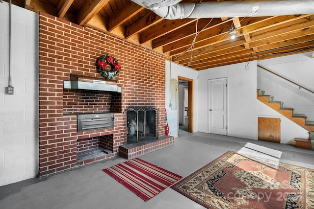 unfurnished living room featuring finished concrete flooring, a brick fireplace, stairs, and concrete block wall