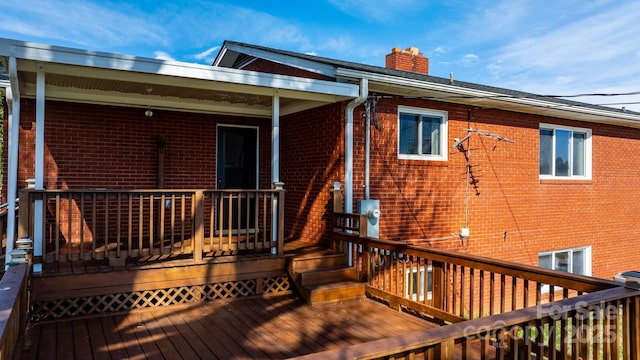 back of house with a chimney, brick siding, and a deck