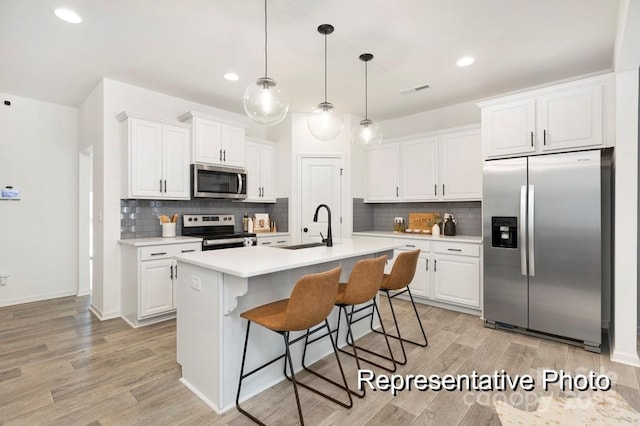 kitchen featuring a kitchen island with sink, sink, stainless steel appliances, and white cabinets