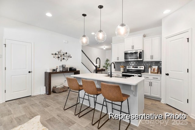 kitchen with white cabinetry, an island with sink, sink, hanging light fixtures, and stainless steel appliances