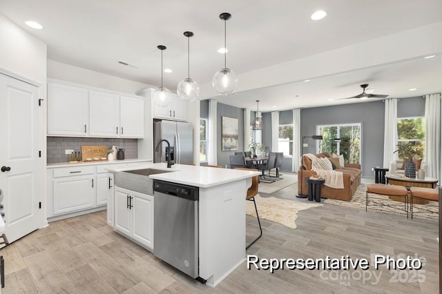 kitchen with pendant lighting, sink, appliances with stainless steel finishes, an island with sink, and white cabinets