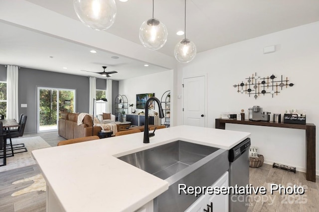 kitchen featuring sink, hanging light fixtures, an island with sink, stainless steel dishwasher, and light wood-type flooring