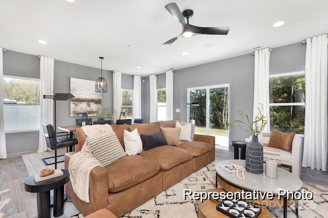 living room with ceiling fan with notable chandelier and light hardwood / wood-style flooring