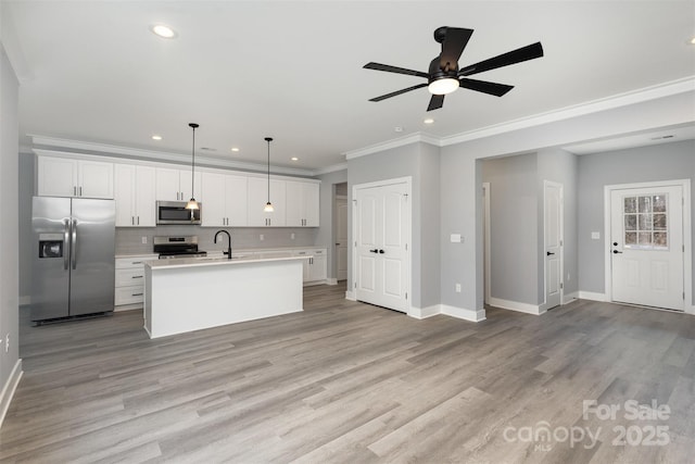 kitchen featuring tasteful backsplash, hanging light fixtures, a center island with sink, stainless steel appliances, and white cabinets