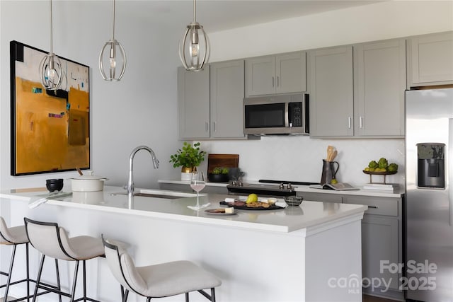 kitchen with a breakfast bar, gray cabinets, a sink, stainless steel appliances, and light countertops