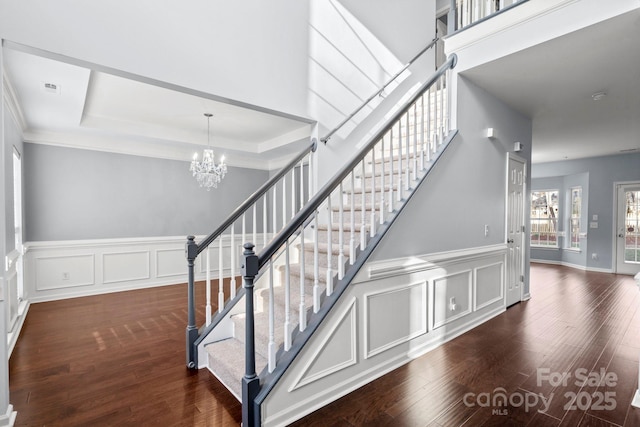 staircase featuring a raised ceiling, wood-type flooring, a notable chandelier, and crown molding