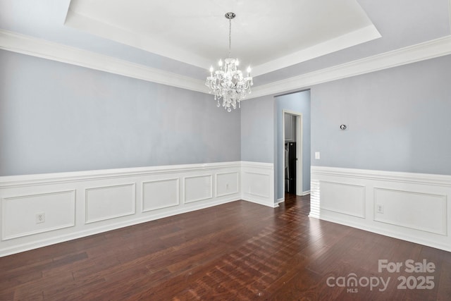 spare room with a raised ceiling, dark hardwood / wood-style floors, and a notable chandelier