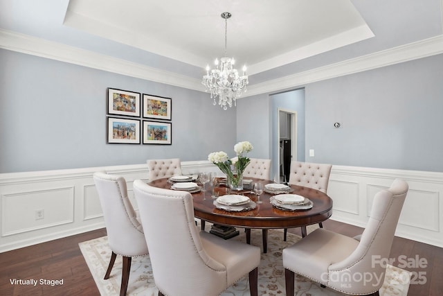 dining space with dark wood-type flooring, a tray ceiling, and a notable chandelier